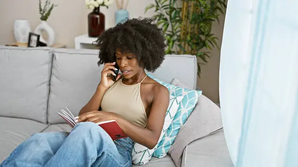 African american woman talking on smartphone reading book at home