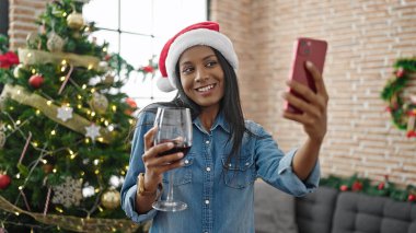 Afro-Amerikalı kadın akıllı telefonla selfie çekiyor evde Noel 'i kutlamak için şarap içiyor.