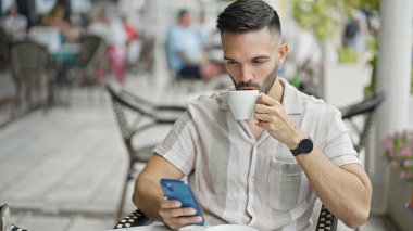 Genç İspanyol adam akıllı telefon kullanıyor. Kahve dükkanının terasında kahve içiyor.