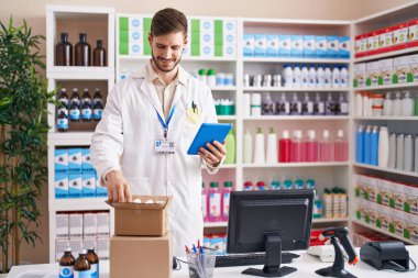 Young caucasian man pharmacist using touchpad holding pills bottle at pharmacy