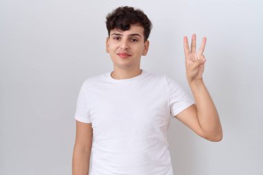 Gündelik beyaz tişört giyen, üç numaralı parmaklarıyla gülümseyerek kendinden emin ve mutlu genç bir adam.. 