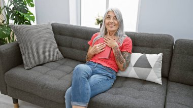 Evde, kendinden emin, gri saçlı, orta yaşlı bir kadın rahat kanepesinde oturuyor, elinde kitap, güzel gülüşü gerçek neşe ve rahatlık saçıyor..