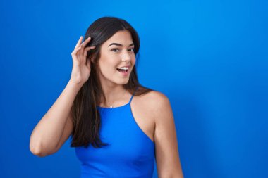 Mavi arka planda dikilen İspanyol kadın kulağına fısıldayarak dedikoduları ve dedikoduları dinliyor. Sağırlık kavramı. 