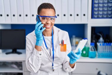 Akıllı telefondan konuşan Afrikalı Amerikalı kadın bilim adamı laboratuarda örnek arıyor.