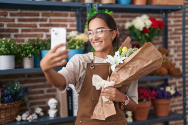 Çiçekçiye elinde çiçeklerle akıllı telefonuyla selfie çeken güzel bir İspanyol kadın.