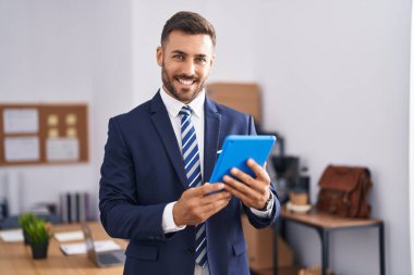 Young hispanic man business worker smiling confident using touchpad at office