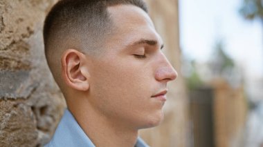 Şehir caddesinde gözleri kapalı ve sakin bir ifadeyle dikilen, günlük kıyafetli yakışıklı İspanyol bir adam..