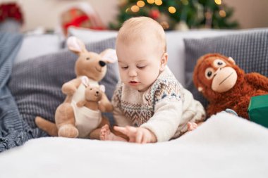 Evdeki gevşek yüzlü, Noel ağacının yanındaki kanepede oturan sevimli beyaz bebek.