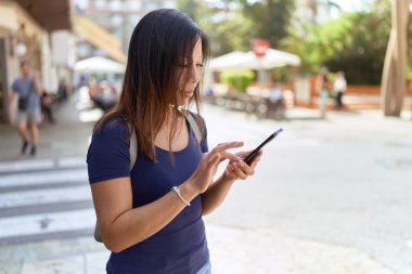 Genç Asyalı bir kadın sokakta akıllı telefon kullanıyor.