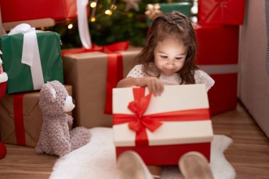 Sevimli İspanyol kız hediyesini açıyor. Evdeki Noel ağacının yanında oturuyor.