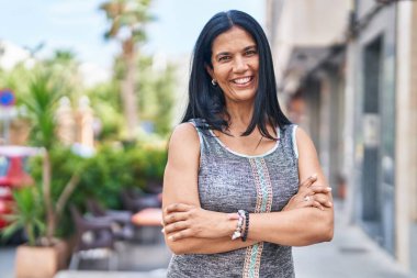 Orta yaşlı İspanyol kadın caddede kollarını kavuşturup el kol hareketi yapıyor.