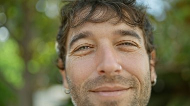 Yakışıklı genç sarışın adam kenar mahallede kendine güvenen ve gülümseyen neşeli ve pozitif görünüyor. Yakın plan portresi neşeli ifadesini ve gülüşünü sergiliyor..