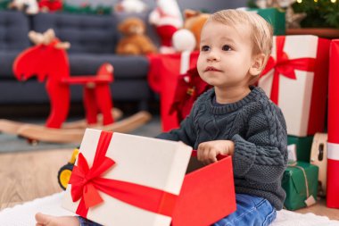 Sevimli sarışın bebek evde oturmuş Noel hediyesini açıyor.