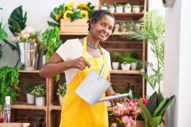 Middle age african american woman florist smiling confident watering plant at flower shop