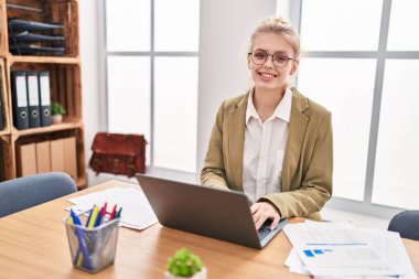 Ofiste çalışan genç sarışın iş kadını dizüstü bilgisayar kullanıyor.