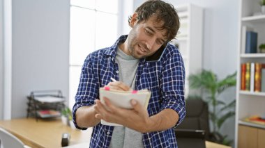 Genç, çalışkan bir adam ofis telefonundan notlar alıp konuşmakla meşgul.