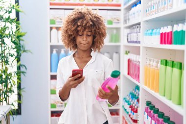 Afrika kökenli Amerikalı kadın müşteri eczanede akıllı telefon şampuanı kullanıyor.
