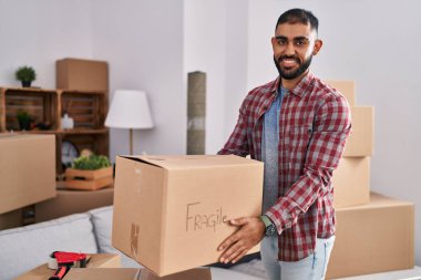 Young hispanic man smiling confident holding fragile package at new home