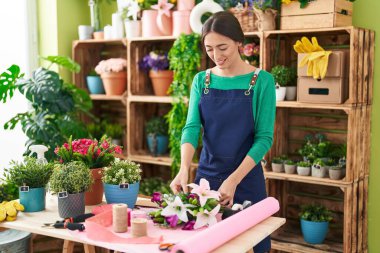 Young beautiful hispanic woman florist make bouquet of flowers at flower shop