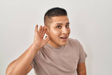 Beyaz arka planda dikilen Latin asıllı genç adam kulağına fısıldayarak dedikoduları ve dedikoduları dinliyor. Sağırlık kavramı. 