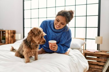 Genç, güzel, İspanyol bir kadın. Bir fincan kahve içiyor. Yatakta köpekle oturuyor.