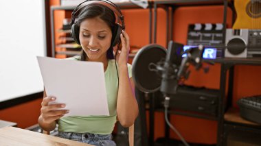 Genç Latin kadın müzisyen gülümsüyor. Müzik stüdyosunda kendine güvenen şarkı söylüyor.