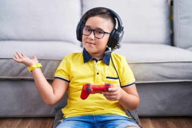 Video oyunu oynayan, kulaklık takan, avuç içlerini açıp fotokopi alanını gösteren, gülümseyen mutlu bir gülümseme sunan İspanyol çocuk. 