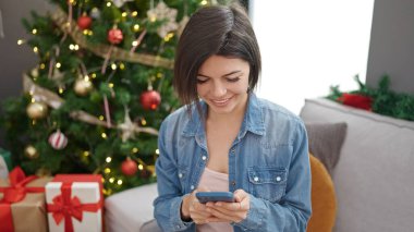 Beyaz kadın akıllı telefon kullanıyor. Evdeki kanepede oturuyor.