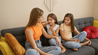 Genç İspanyol anne, rahat bir oturma odasında gri bir kanepede oturan kızlarıyla konuşuyor.
