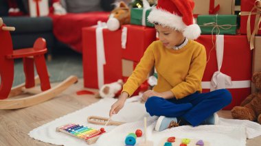 Adorable hispanic boy playing xylophone sitting on floor by christmas gifts at home