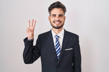 Dövmeli, takım elbiseli ve kravatlı genç İspanyol adam üç numaralı parmaklarıyla kendini beğenmiş ve mutlu gülümserken kendini gösteriyor.. 
