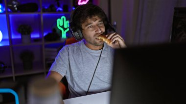 Kulaklıklı bir adam geceleri neon ışıklı bir odada oyun oynarken yemek yer, eğlence ve teknolojiyi temsil eder..