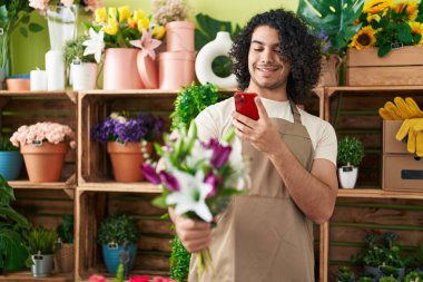 Genç latin çiçekçi çiçekçide çiçekçide akıllı telefonla fotoğraf çekiyor.