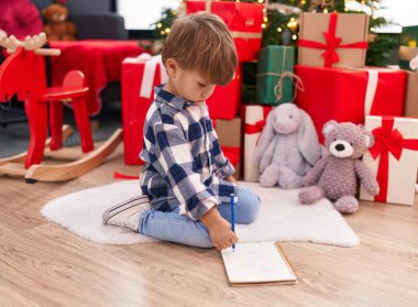 Sevimli İspanyol çocuk Noel Baba mektubu yazıyor. Noel ağacının yanında oturuyor.