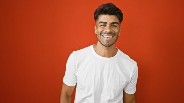 Sakallı yakışıklı genç adam, kırmızı izole bir arka plana gülümsüyor..