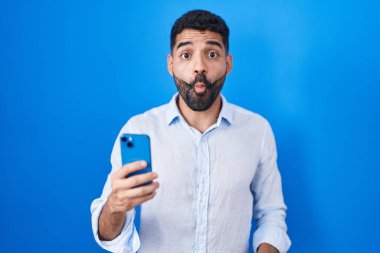 Sakallı İspanyol adam akıllı telefon kullanarak mesaj yazıyor. Dudaklarıyla balık suratı yapıyor. Çılgınca ve komik bir jest. Komik ifade. 