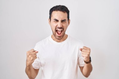 Beyaz arka planda duran yakışıklı İspanyol adam kızgın ve kızgın bağırıyor sinirli ve öfkeli, öfkeyle bağırıyor. öfke ve agresif konsept. 