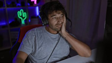 Geceleri karanlık bir oyun odasında dinlenen sakallı, yorgun İspanyol bir adam teknoloji ve yaşam tarzı sergiliyor..