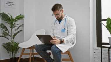Genç İspanyol doktor, klinik bekleme odasında dizüstü bilgisayar kullanıyor.