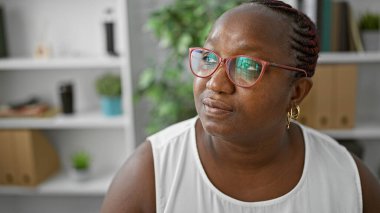 Odaklanmış Afro-Amerikan iş kadını, düşünceli, başarılı bir işçi ofis yan odasında fikirler üzerinde kafa yoruyor, şüphe ederken kendine güveni artıyor.