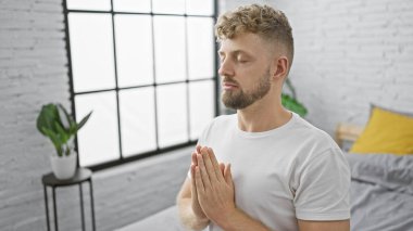 Yakışıklı beyaz adam, huzurlu, modern bir yatak odasında gözleri kapalı meditasyon yapıyor..