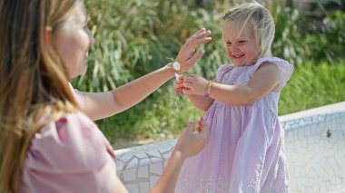 Neşeli beyaz anne ve küçük kızı bir bankta birlikte oturuyor, elinde bir çiçek, neşe ve güven saçıyor.