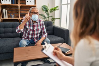 Tıbbi maskeli son sınıf öğrencisi, bir psikoloji kliniğinde mutlu bir yüzle işaret ederek, 