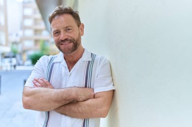 Orta yaşlı bir adam caddede kollarını kavuşturmuş duruyor.