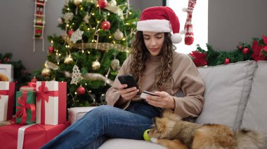 Akıllı telefon ve kredi kartıyla köpek alışverişi yapan genç İspanyol kadın Noel 'i evde kutluyor.