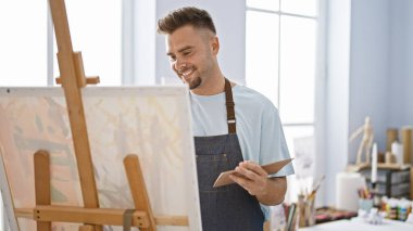 Parlak bir sanat stüdyosunda resim yapan gülümseyen bir adam..