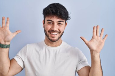 Hispanic man with beard standing over white background showing and pointing up with fingers number ten while smiling confident and happy. 