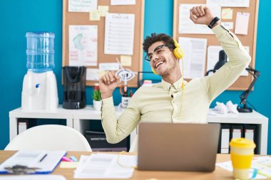 Young hispanic man business worker listening to music and dancing at office