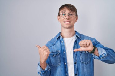 Beyaz tenli, sarışın, gözlüklü, arkasını gösteren, elleri havada, kendinden emin, gülümseyen bir adam. 