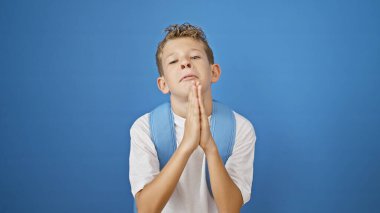 Sevimli sarışın öğrenci, bir jest yaparak el ele tutuşuyor, parlak mavi bir arka plana karşı tek başına duruyor.